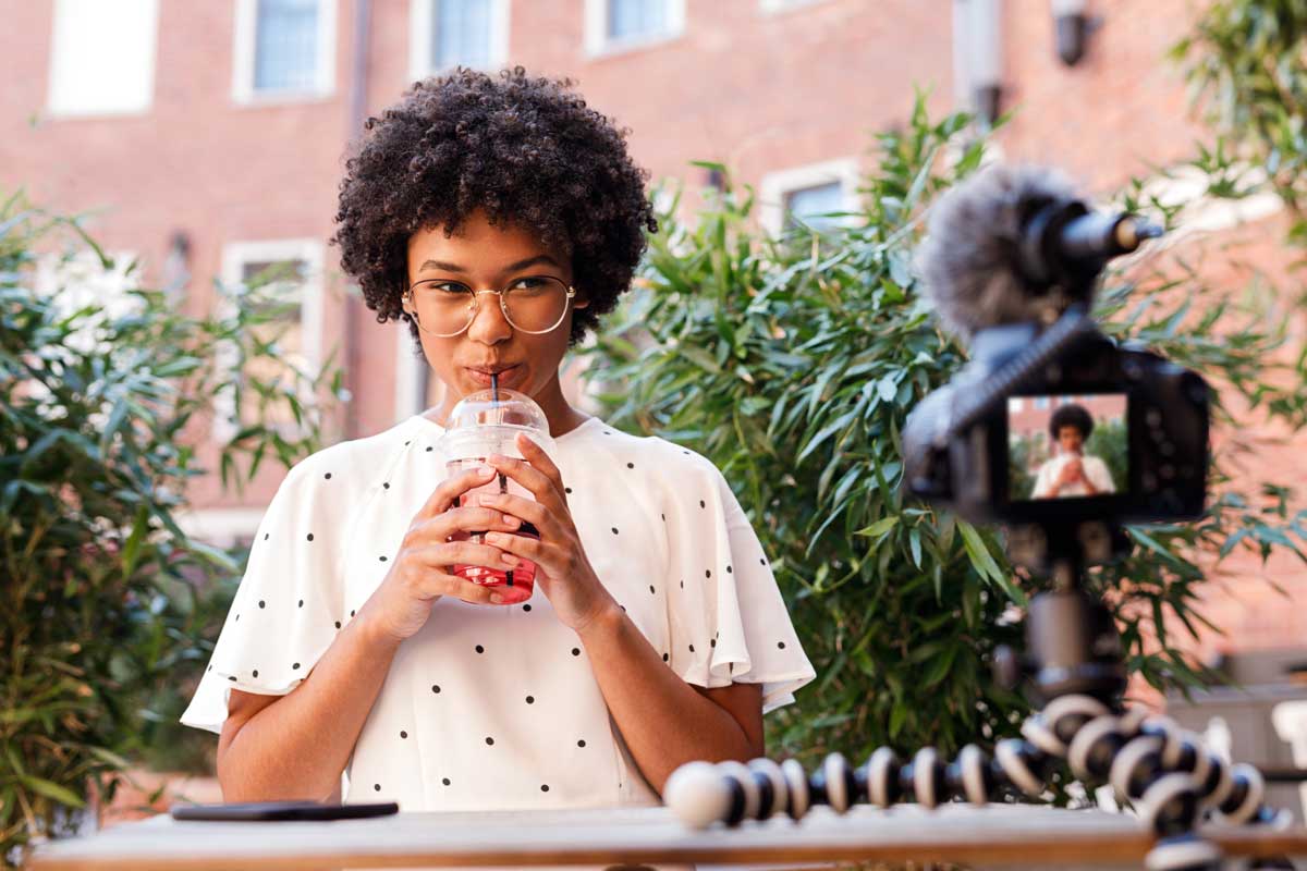 A woman drinking a beverage while facing the camera and recording a video for content marketing on social media.