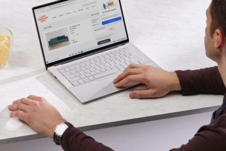 A person using a laptop to shop for a sofa on an online store named 'Super Shopping Now'