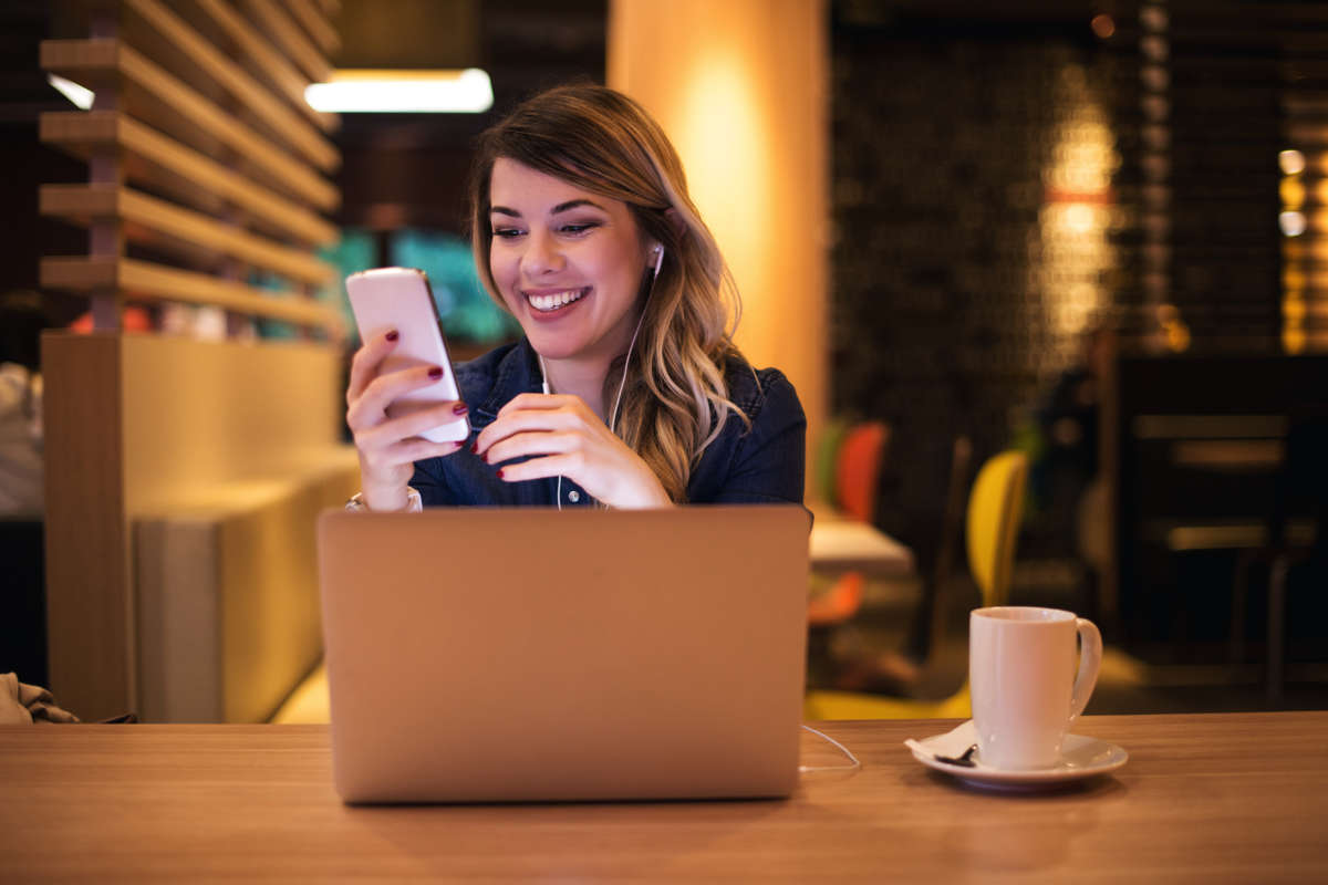happy social media assistant working on a laptop and looking at their phone
