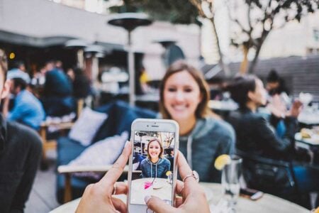 Social media enthusiast taking a photo of a friend at an outdoor restaurant, using an iPhone to create engaging content